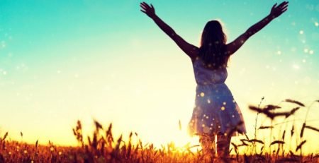Woman with arms raised in a golden field at sunset representing comfort and wellbeing