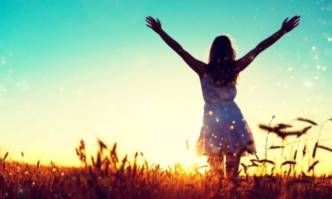 Woman with arms raised in a golden field at sunset representing comfort and wellbeing