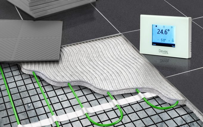 Cross-section of electric underfloor heating mat installed under dark floor tiles with Devex TS-500 thermostat