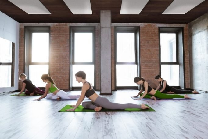 Group of women practising yoga on green mats in a bright studio with warm timber floors, showing Comfortline Slimline heater application