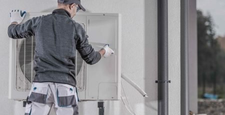 Technician installing heat pump outdoor unit on residential home exterior wall