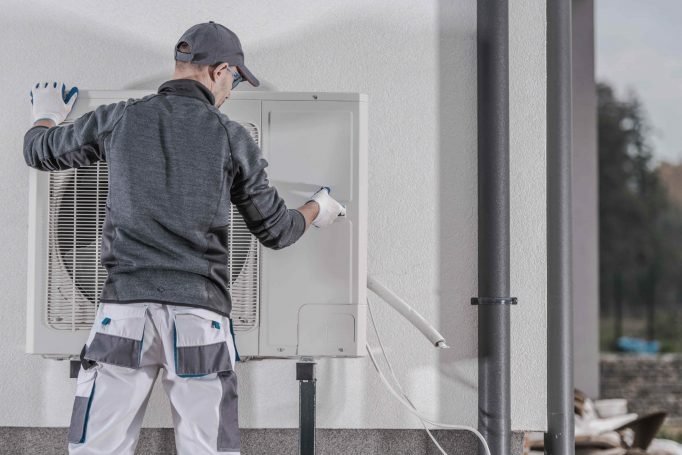 Technician installing heat pump outdoor unit on residential home exterior wall