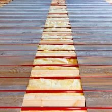 Aluminium heat diffusion plates installed over hydronic pipes in a timber subfloor