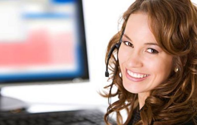 Smiling customer service representative wearing headset at computer workstation