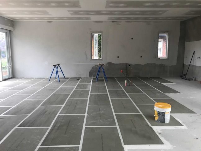 Underfloor heating installation in progress with heating cables laid in a grid pattern across a concrete subfloor