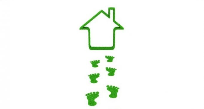 Eco-friendly home concept with green footprints leading to a grass house outline
