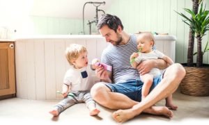 Father sitting on a warm bathroom floor with two young children, illustrating family comfort with underfloor heating