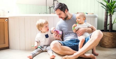 Father sitting on a warm bathroom floor with two young children, illustrating family comfort with underfloor heating