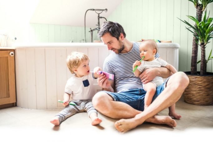 Father sitting on a warm bathroom floor with two young children, illustrating family comfort with underfloor heating