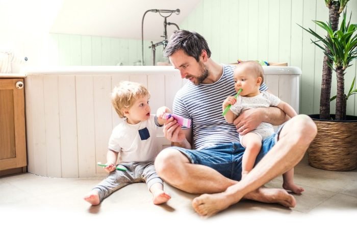 Father sitting on a warm bathroom floor with two young children, illustrating family comfort with underfloor heating